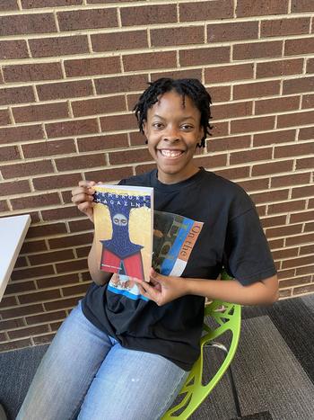 Woman sitting at a table holding up a copy of Pembroke magazine